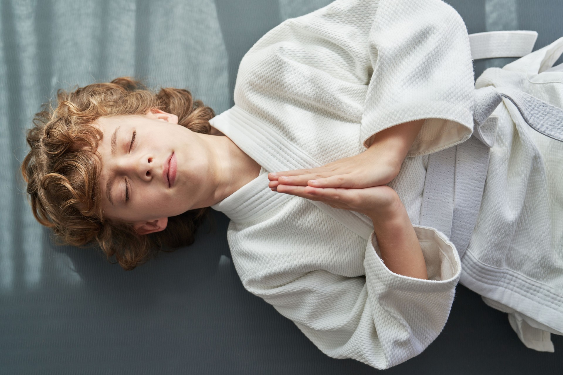 Boy in kimono lying on floor and doing namaste gesture